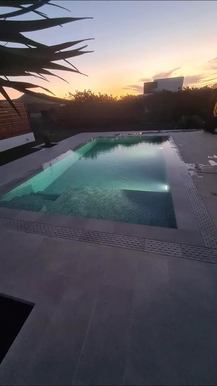 Piscina de revestimiento oscuro con rejilla perimetral y agua esmeralda