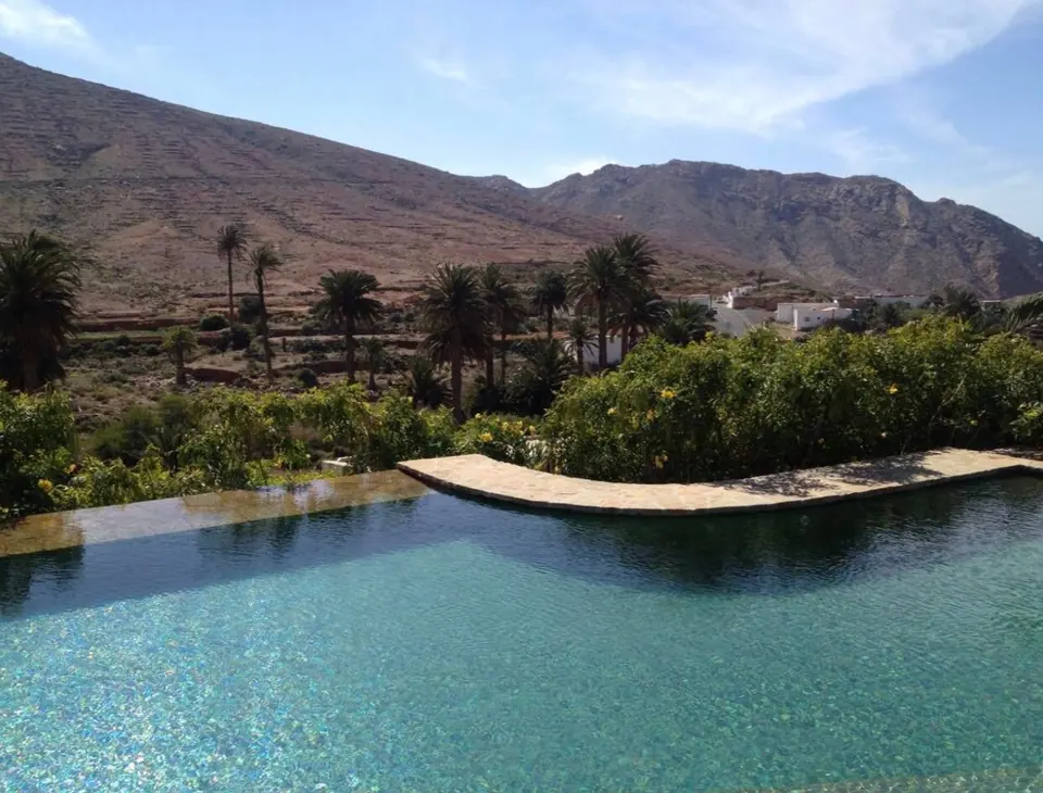 Piscina desbordante con vistas a un palmeral y montañas volcánicas de Fuerteventura