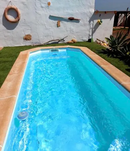 Piscina de esquinas redondeadas con coronación de piedra y jardín