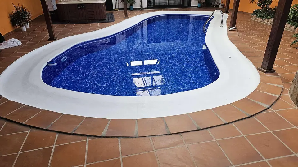 Piscina de forma libre con gresite azul y coronación blanca