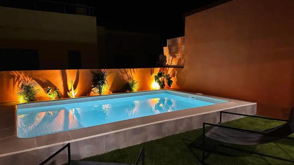 Piscina rectangular iluminada de noche con focos LED y jardín