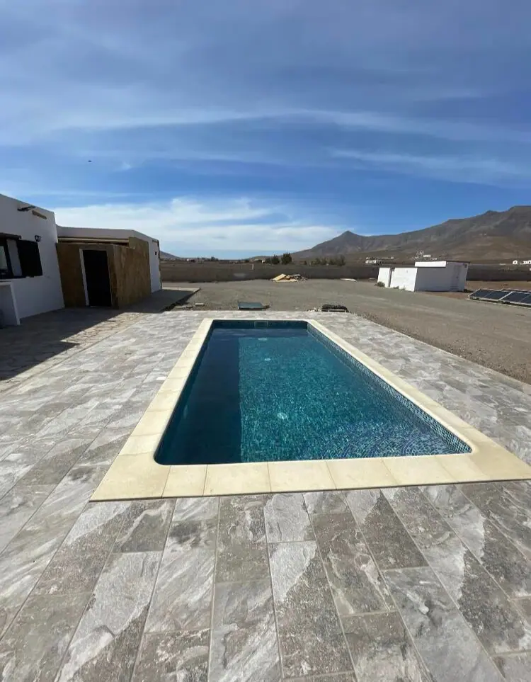 Piscina rectangular con coronación de piedra y montañas de Fuerteventura al fondo
