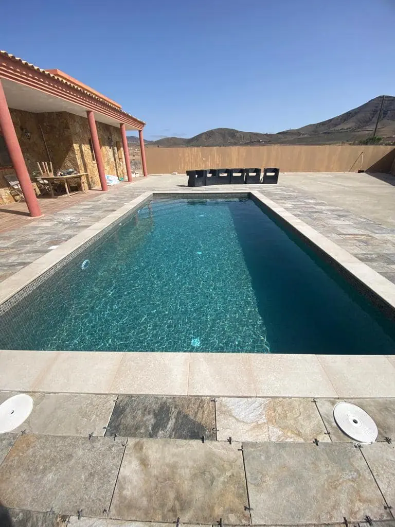 Piscina rectangular alargada con revestimiento gris y playa de piedra clara