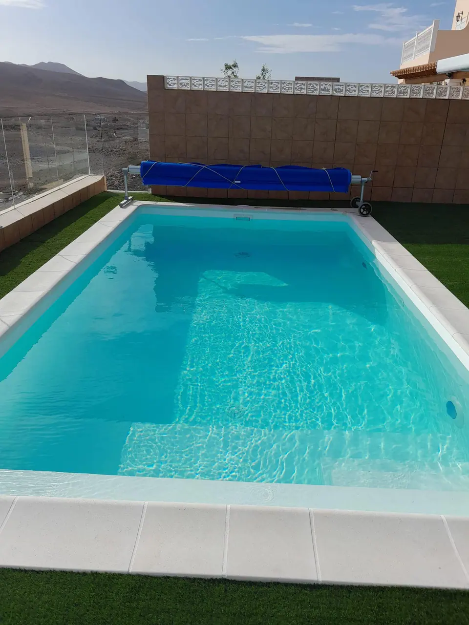 Piscina rectangular de agua turquesa con escalera y césped artificial