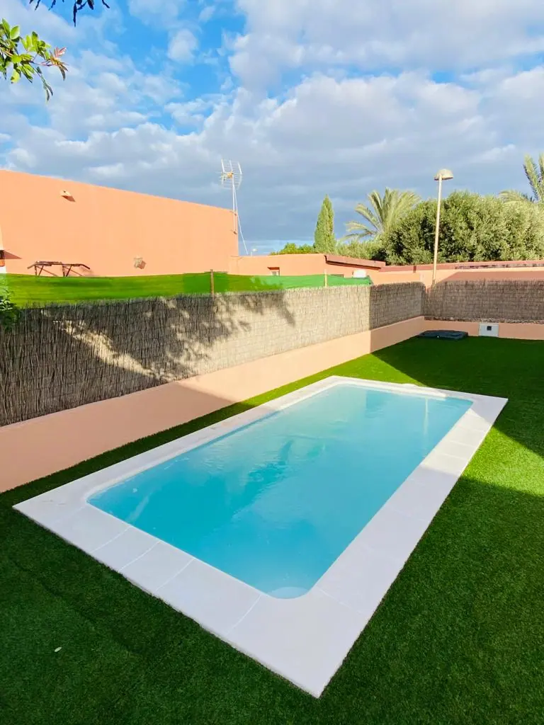 Piscina con muro de piedra volcánica y césped artificial