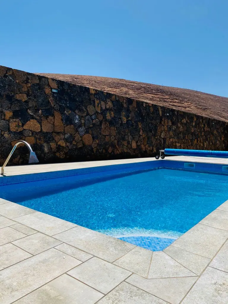 Piscina con muro de piedra volcánica y ducha de acero inoxidable